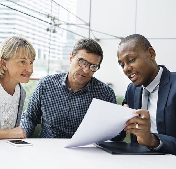 A man in a suit is reviewing a document with two older people, presumably a couple, in an office filled with windows and natural light